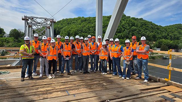 Group of students and faculty in orange safety vests standing on a bridge