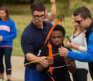 UW-Platteville students assisting student with archery