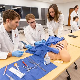 A group of biology students practice medical techniques in lab
