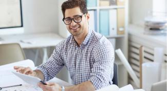 Smiling engineering student wearing glasses, seated at a desk reviewing papers in a bright office.