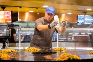 UW-Platteville dining staff in blue shirt pointing and cooking on large grill