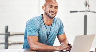 Smiling sport administration student on laptop with lat pull machine in background