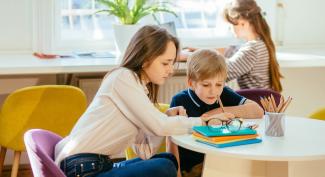 A social worker works one-on-one with a child, while another child works in the background.