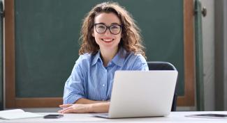 Smiling young educator working at desk on laptop