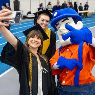 UW-Platteville graduates smile and take a selfie with Pioneer Pete.