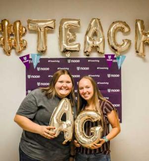 Two smiling students holding balloons of the letters A and G with #Teach above them