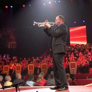 Jon Schipper standing on stage playing trumpet to large crowd of people