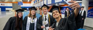 Four UW-Platteville students in black caps and gowns taking a selfie together at the graduation commencement ceremony.