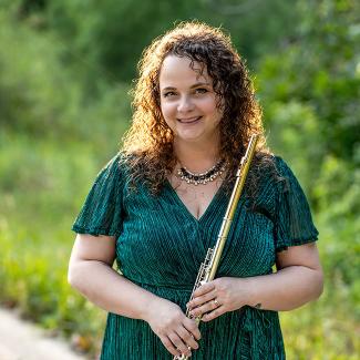 Rose Bishop smiles while standing outdoors, wearing a green dress and holding a flute