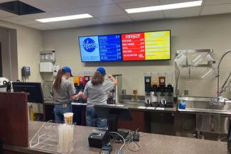 Two baristas in gray shirts using coffee machines at Hickory and Main.