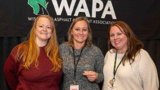 Three women posing in front of dark backdrop that reads WAPA