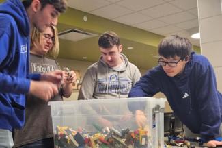 Four individuals looking down and reaching into a large bin of lego bricks.