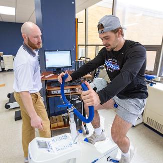 Athlete using a stationary bike with guidance from a trainer in a fitness facility.
