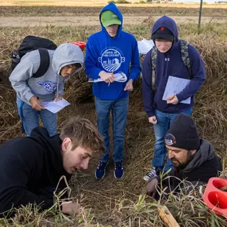Students conducting a soil analysis in a field, observing samples and taking notes.
