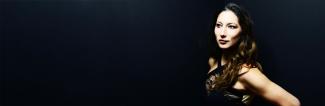 Woman with long dark hair, looking off to the side in front of a black background.